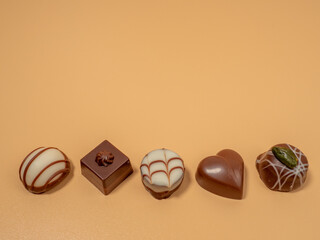 Assorted gourmet pralines in white, dark and milk chocolate. Chocolate candies on an orange background.