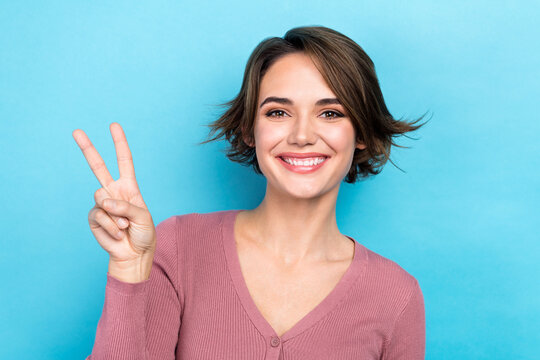 Photo of cheerful shiny lady wear pink cardigan showing v-sign smiling isolated blue color background