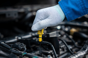 Mechanic checking car oil level with a gauge while standing next to an open hood. Expert examining engine oil for maintenance and safety purposes.