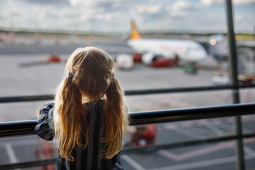 Fototapeta na wymiar Little girl at the airport waiting for boarding at the big window. Cute kid stands at the window against the backdrop of airplanes. Looking forward to leaving for a family summer vacation
