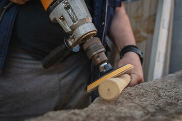 A man is using power tool to polish wooden stick
