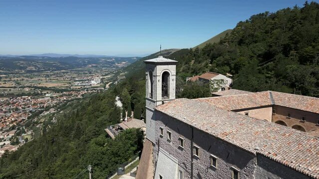 Cinematic aerial view of hillside Catholic church overlooking the picturesque town of Gubbio, Italy.