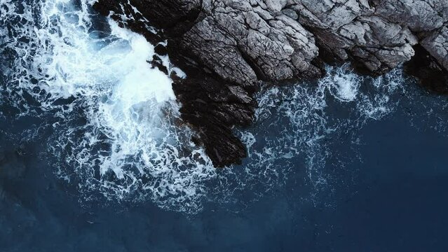 Drone above of turquoise ocean waves crashing and white foaming on huge reef rock stones. Wild sea washing reef rock cliff