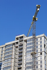 Fototapeta premium Construction site. Reinforced concrete frame of a multi-storey building and construction cranes. The final stage of construction. Against the background of the blue sky.