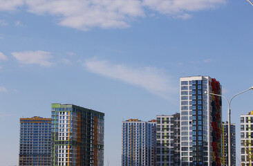 Fototapeta premium Modern high-rise buildings made of concrete and glass. Color design of facades. Construction site. The final stage of construction. Against the background of the blue sky.