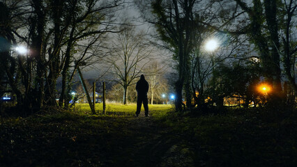 A threatening mysterious hooded figure. Silhouetted by street lights on the edge of town. Standing...
