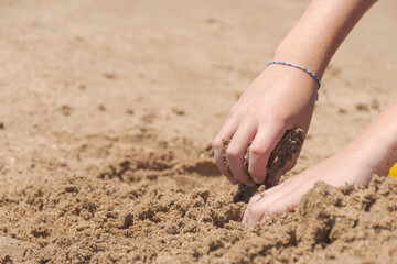 Hands of a child playing with sand on the beach.