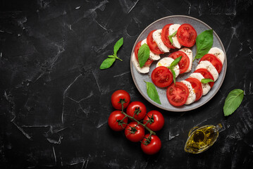 Italian caprese salad with chopped tomatoes, mozzarella, basil, olive oil on a black stone background. Top view, flat lay