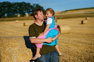 Little girl in traditional Bavarian costume and father in wheat field. Happy child and dad with hay...