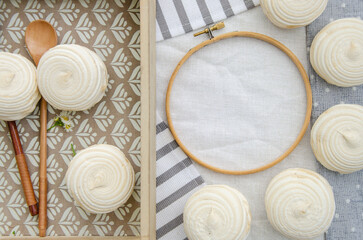 Fototapeta na wymiar Meringue homemade zephyr marshmallows in a wooden tray with wooden spoons and round embroidery hoop frame on cotton tablecloth. Mockup card. Template for recipes book or food menu