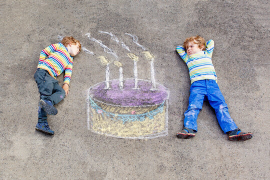 Two happy little kids having fun with big birthday cake picture drawing with colorful chalks. Creative leisure for children outdoors in summer. Kids blowing candles