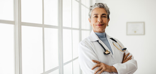Senior doctor in a lab coat standing with her arms crossed, inspiring trust and confidence