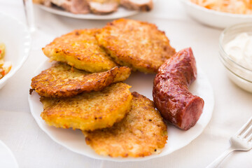 Fried grated potato pancakes with fried sausage on white plate