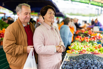 Happy mature couple picking fresh blueberries during shopping together at local market