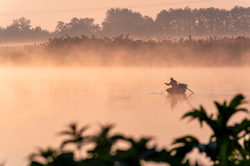 Obraz na płótnie Canvas a fisherman casting nets on a boat into the river at dawn.