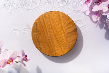 Wooden podium or pedestal of water ripples and orchid flowers lying flat, top view. Summer cosmetic template, mockup