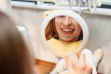 Using mirror to look at aligner on teeth. Woman in the stomatology clinic, visiting dentist