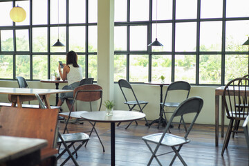 Rear view of womansits in the coffee shop with empty wooden furniture