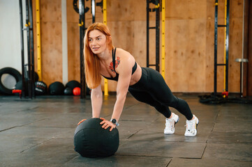 Doing push ups by using soft ball. Beautiful strong woman is in the gym