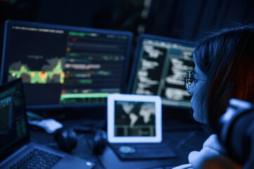 Phishing attack. Young professional female hacker is indoors by computer with lot of information on displays