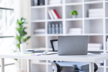 Laptop Computer, notebook, and eyeglasses sitting on a desk in a large open plan office space after working hours	