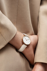 Beautiful luxury women's watch with a white leather strap on the wrist of a woman wearing a beige coat or jacket. Advertisement of a popular watch
