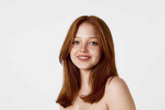 Portrait of young, beautiful, tender redhead girl with well-kept face and straight hair looking at camera against white background. Natural beauty, hair care, cosmetology, cosmetics, skin care concept