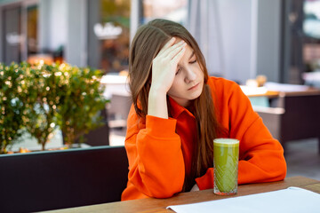 teen girl is upset. unhappy girl does not want to drink green tasteless vegetable juice in cafe