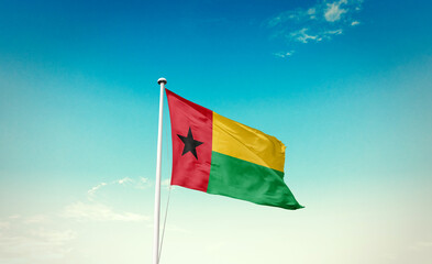 Waving Flag of Guinea-Bissau in Blue Sky. The symbol of the state on wavy cotton fabric. - obrazy, fototapety, plakaty