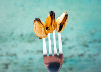 Fresh mussels on a fork on a blue sea background close-up, healthy sea product mussels without shells. A man eats a mussel in a restaurant. Pickled - obrazy, fototapety, plakaty