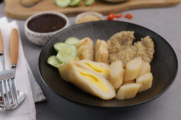 Pempek Palembang, an Indonesian traditional cuisine made from fish cake served with sweet spicy sour sauce and diced cucumber. Piled on white plate on the table