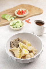 Pempek Palembang, an Indonesian traditional cuisine made from fish cake served with sweet spicy sour sauce and diced cucumber. Piled on white plate on the table