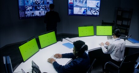 Multiracial officers control security cameras. Workers in monitoring control center. Big digital...