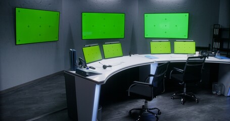 Workspace in security control center for monitoring CCTV cameras. Computer monitors on the table and big digital screens on the wall with chroma key showing surveillance cameras footage. Green screen.