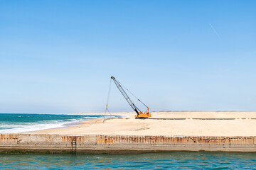 Crane and machine on seashore near blue sea