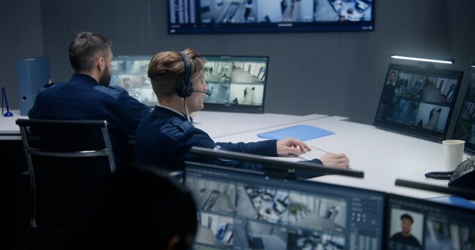 Female security officer watches security cameras with AI facial recognition with male colleagues. Monitoring center workers. Computer monitors and big digital screens with CCTV cameras video footage.