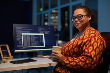 Portrait of African American woman with coffee cup looking at camera while working in IT office...