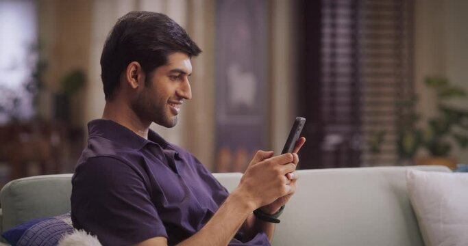 Indian Man Using Smartphone at Home: Engaging in Social Media, Discovering New Music, Learning New Skills through Online Courses, and Embracing the Power of Technology. Medium Shot SLow motion