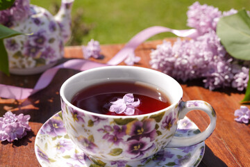 Spring composition with a purple cup with flowers on it,  teapot and lilac flowers on light background.  Tea drinking. Menu, greeting card. 
Spring time. The concept of 'Good morning'