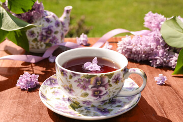 Fototapeta na wymiar Spring composition with a purple cup with flowers on it, teapot and lilac flowers on light background. Tea drinking. Menu, greeting card. Spring time. The concept of 'Good morning'