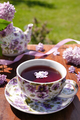 Spring composition with a purple cup with flowers on it,  teapot and lilac flowers on light background. Close up. Tea drinking. Menu, greeting card. Spring time. The concept of 'Good morning' 