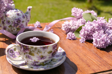 Spring composition with a cup of tea, teapot and lilac flowers on light background. Spring tea party, tea drinking. Menu, greeting card. Side view, copy space for text, product place.