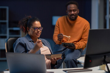 Programmers having lunch while discussing computer program on computer in dark office