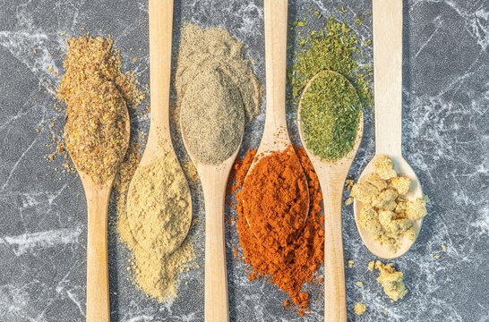 Herbal spices for food preparation in wooden spoons on a marble background