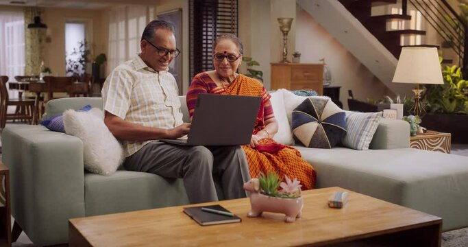 Elderly Couple Using Laptop at Home: Engaged in Joint Online Activities, from Researching Travel Destinations to Sharing Memorable Photos. Happy Older Couple Enjoying Retirement Actively. Medium