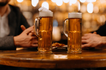 two glasses of beer in the hands of men, friends in a bar, an evening in a pub, close-up