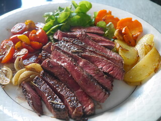 Close-up of a plate of raw, semi-cooked beef steak and a side dish of carrots, tomatoes, on a plain white plate Suitable for making menus in restaurants