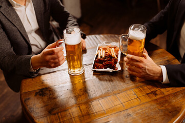 two glasses of beer in the hands of men, friends in a bar, an evening in a pub, close-up