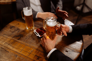 two glasses of beer in the hands of men, friends in a bar, an evening in a pub, close-up