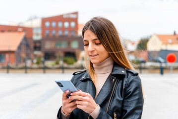 Young hipster woman using a smartphone in the city.female blogger typing text message on her cellphone.Spring day.